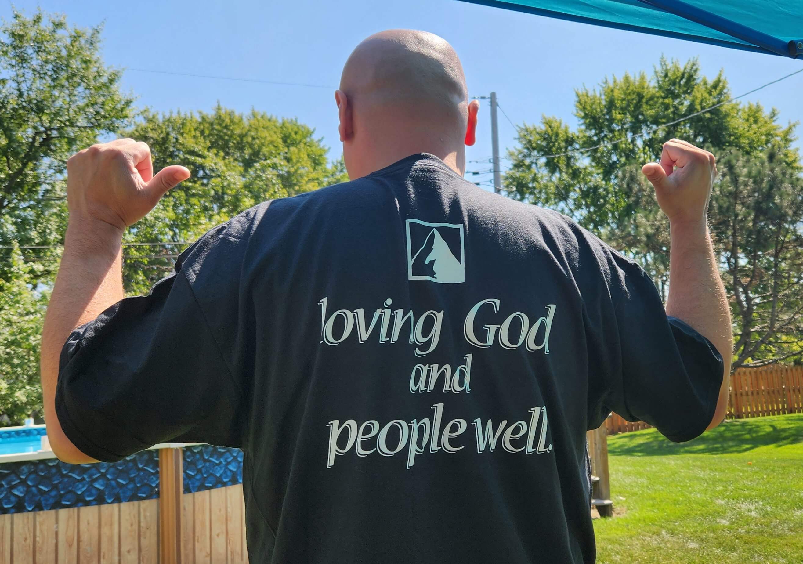 Man wearing a black shirt with a religious message outdoors.