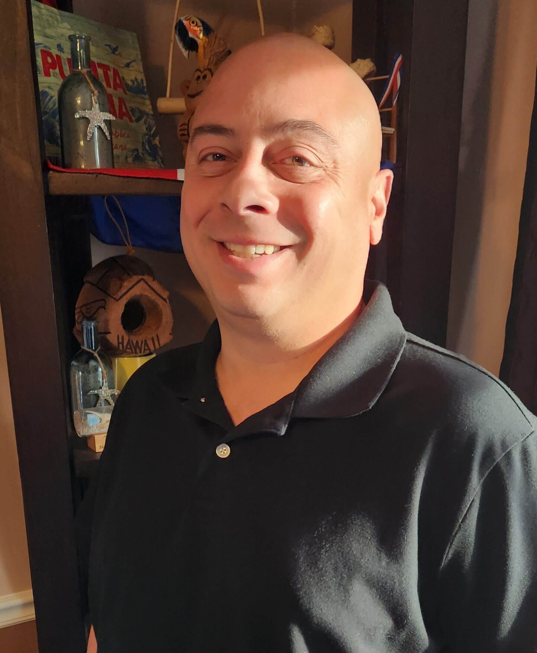 Smiling man in a black polo shirt indoors.