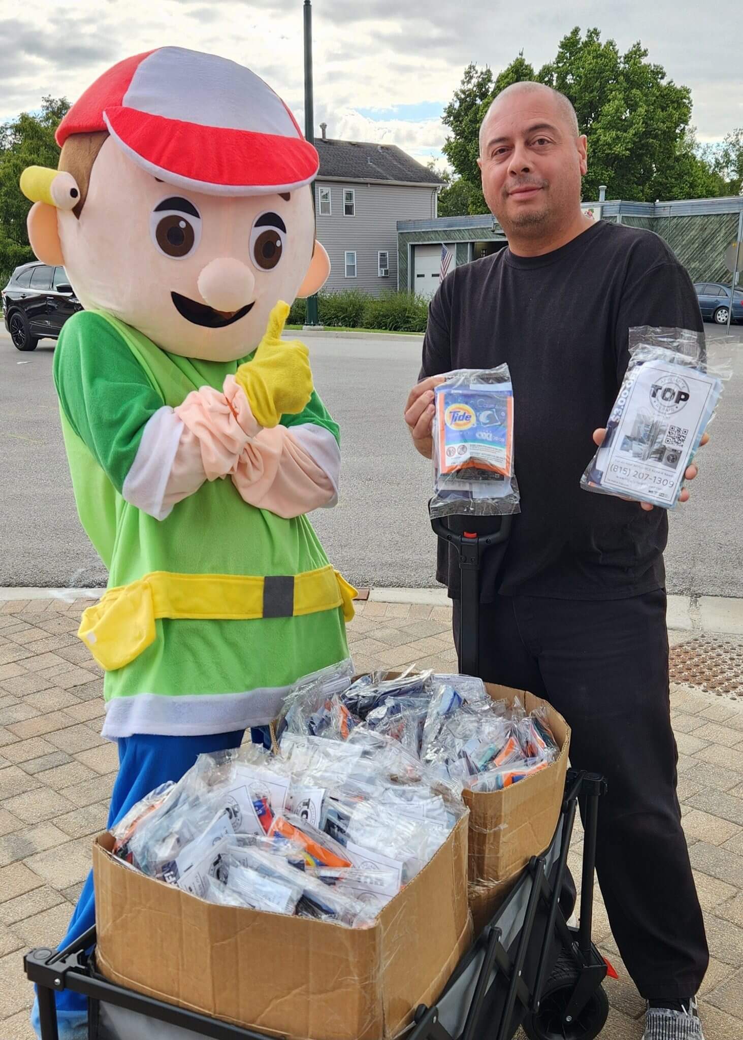 Person and mascot holding packaged items near a basket full of similar goods.