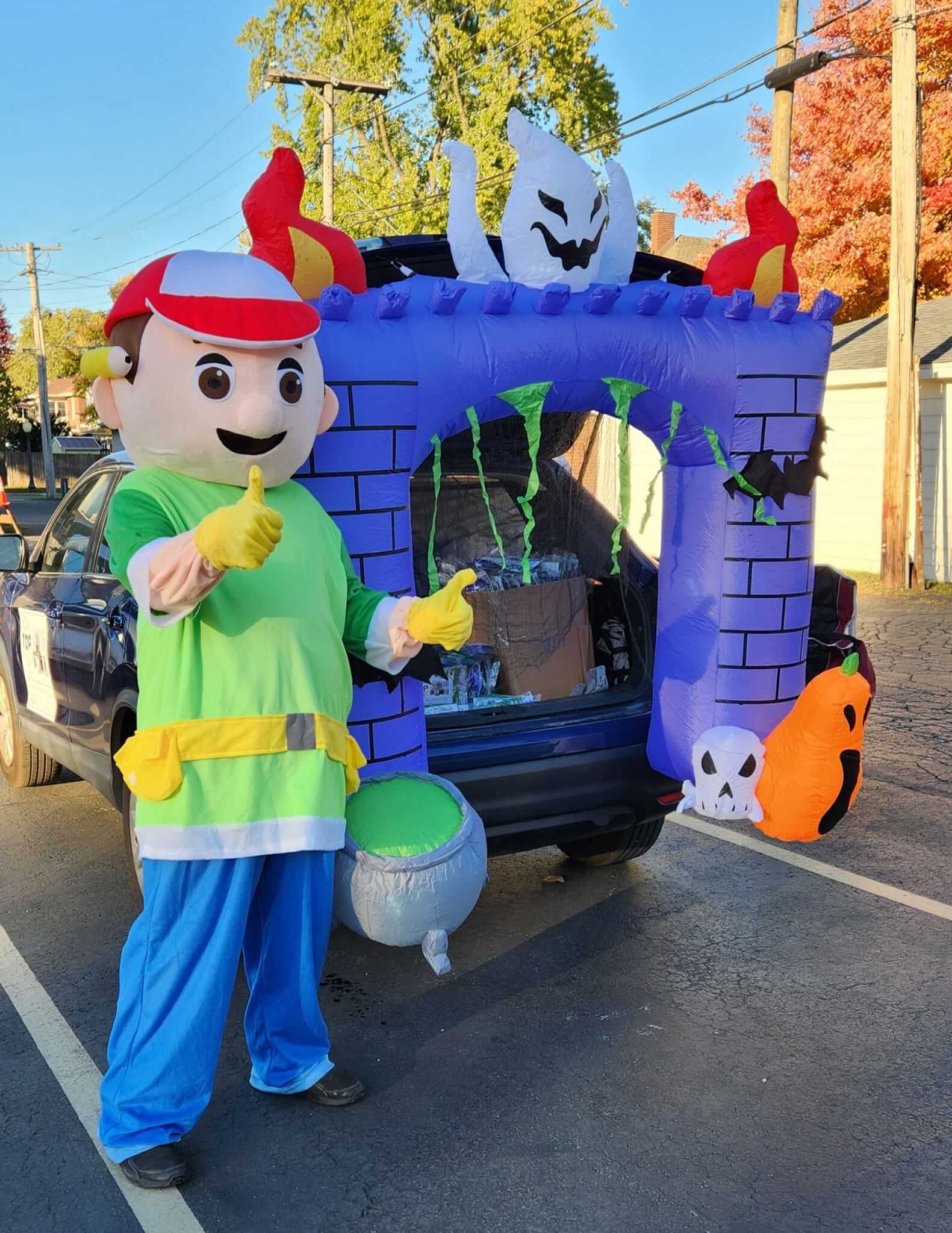Person in colorful costume standing next to a festive Halloween display.
