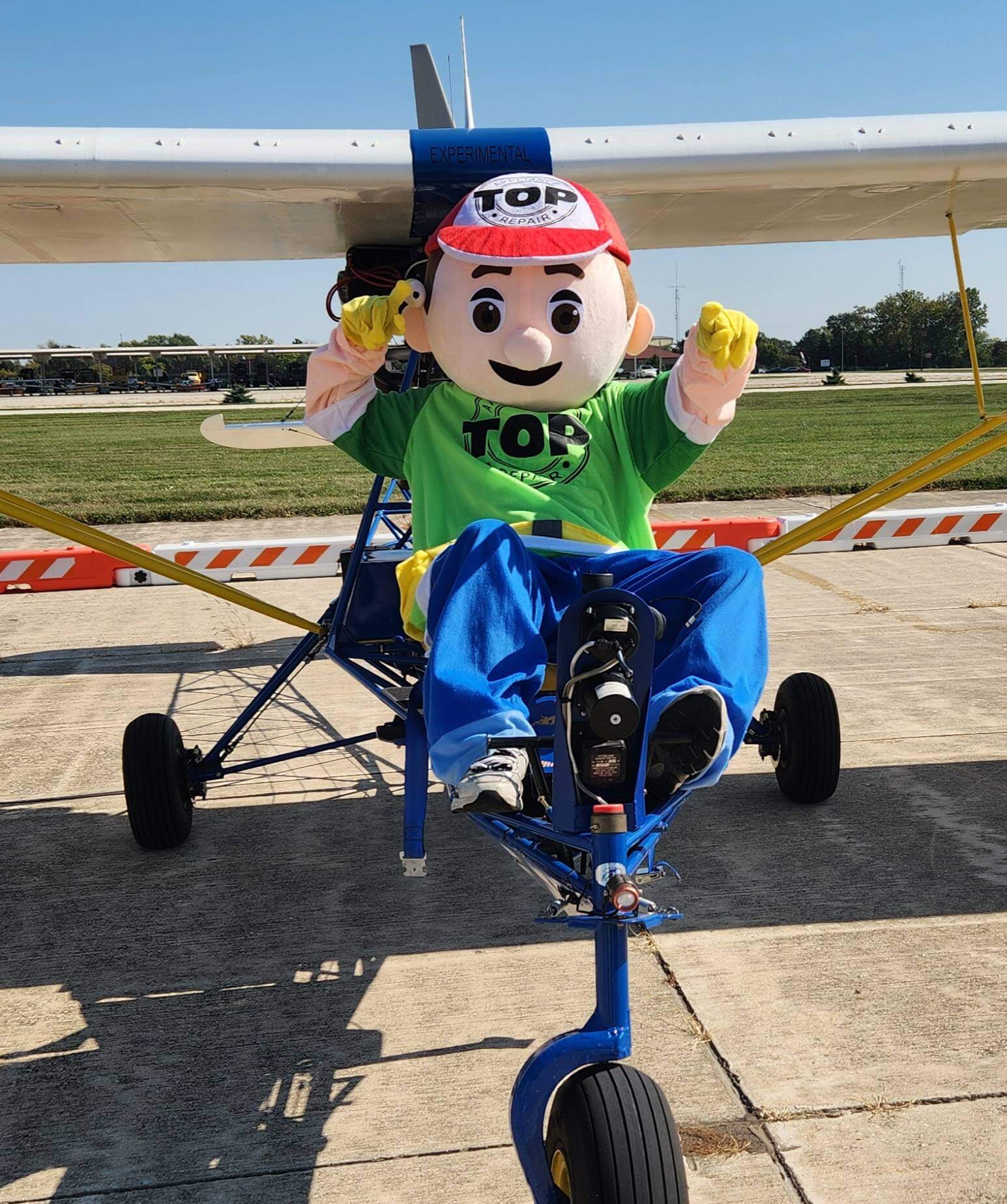 Person in colorful mascot costume posing on a small blue airplane.