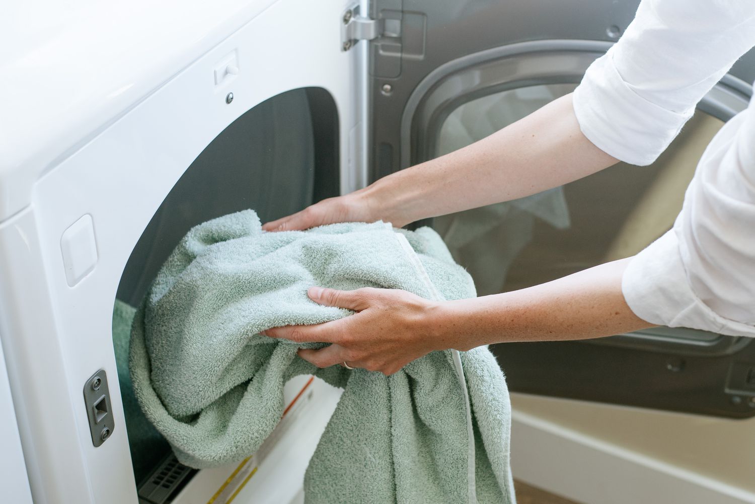Person loading a washing machine with clothes.