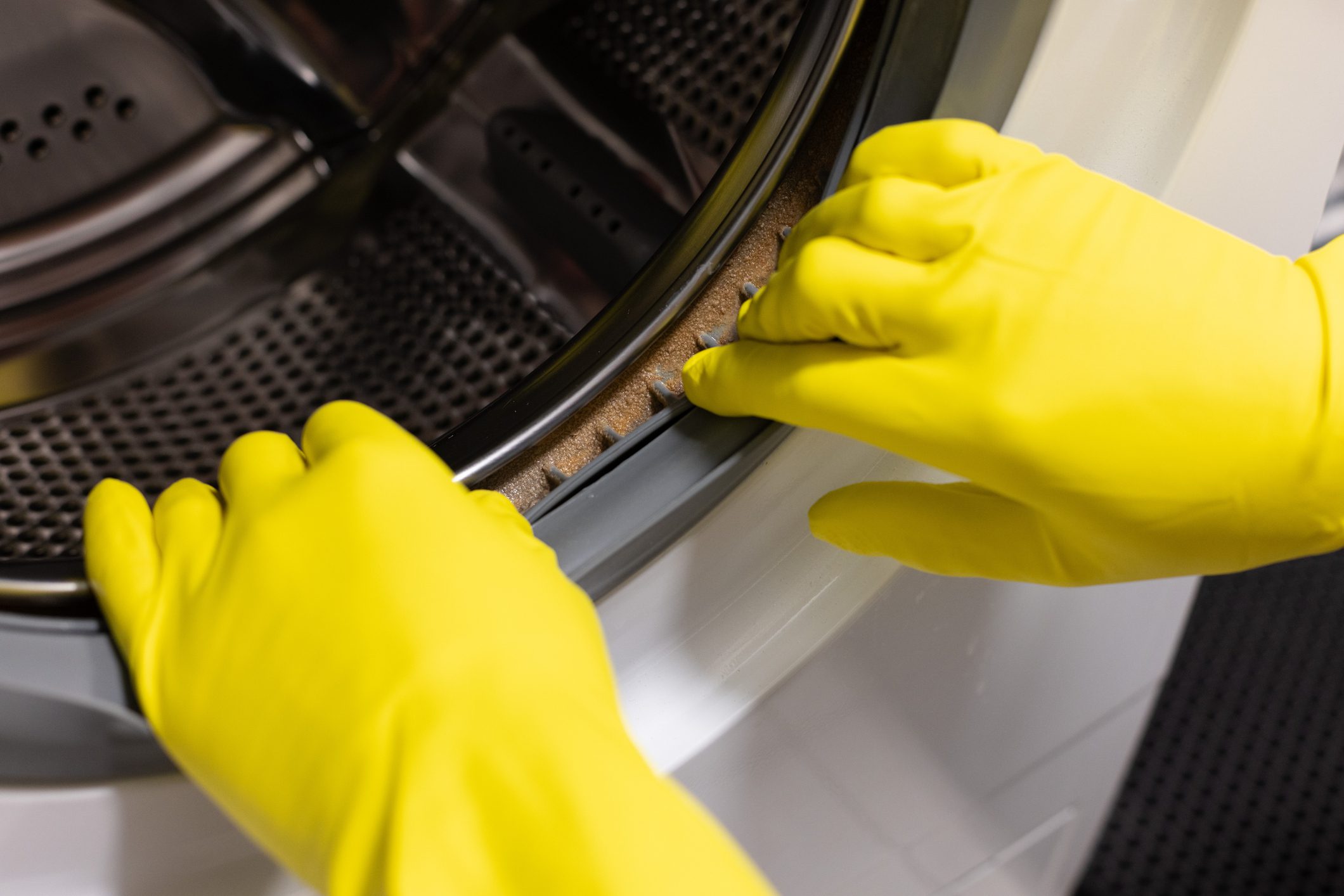 Hands in yellow gloves fixing a washing machine door seal.