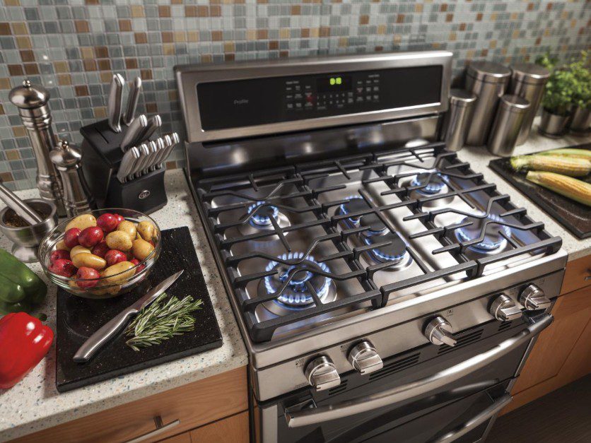 Modern kitchen stove with gas burners and a bowl of apples on the counter.