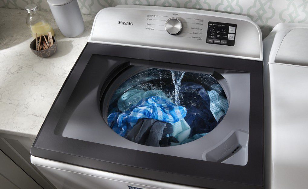 Top-load washing machine with clothes and water inside.